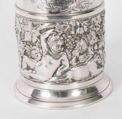 fig 4. A Victorian silver-plated mug featuring embossed putti and grapevine motifs, an engraved rim, a pint capacity mark, and a naturalistic branch-shaped handle.