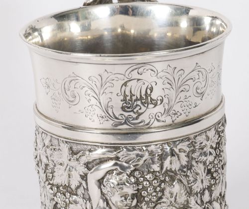 fig 5. A Victorian silver-plated mug featuring embossed putti and grapevine motifs, an engraved rim, a pint capacity mark, and a naturalistic branch-shaped handle.