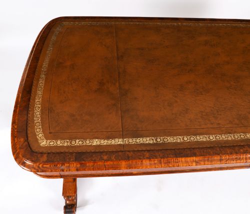 fig 2. A 19th-century Victorian pollard oak writing table featuring a brown leather inset top, carved trestle end supports, a turned central stretcher, and scroll feet on brass castors.