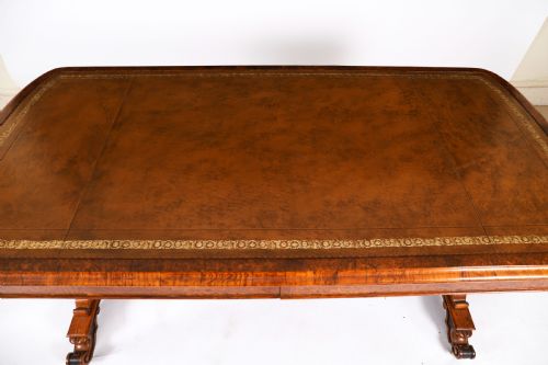 fig 4. A 19th-century Victorian pollard oak writing table featuring a brown leather inset top, carved trestle end supports, a turned central stretcher, and scroll feet on brass castors.