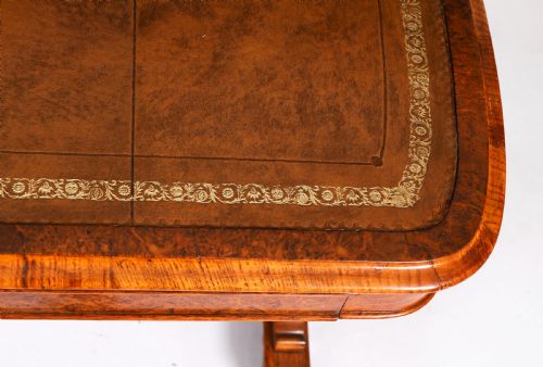 fig 5. A 19th-century Victorian pollard oak writing table featuring a brown leather inset top, carved trestle end supports, a turned central stretcher, and scroll feet on brass castors.