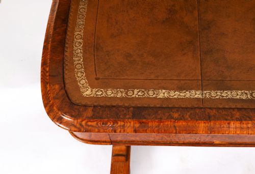 fig 6. A 19th-century Victorian pollard oak writing table featuring a brown leather inset top, carved trestle end supports, a turned central stretcher, and scroll feet on brass castors.