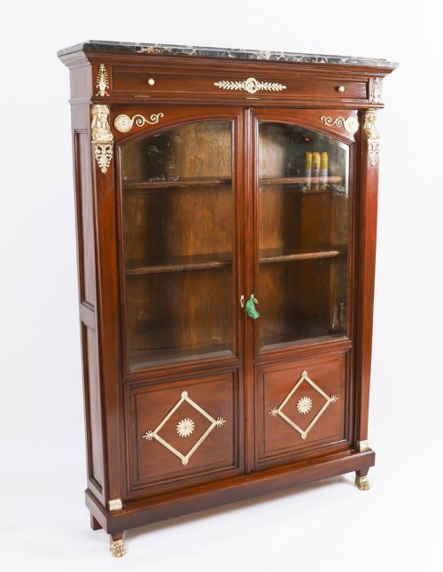 fig 1. A nineteenth-century French Empire Revival mahogany bookcase featuring twin glazed doors, gilt bronze mounts, a marble top, and metal paw feet.