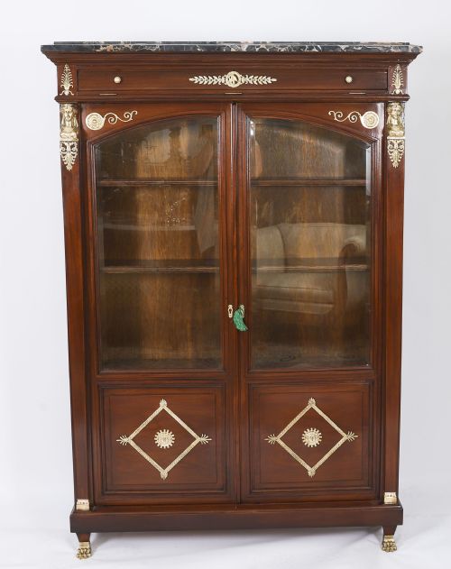 fig 2. A nineteenth-century French Empire Revival mahogany bookcase featuring twin glazed doors, gilt bronze mounts, a marble top, and metal paw feet.
