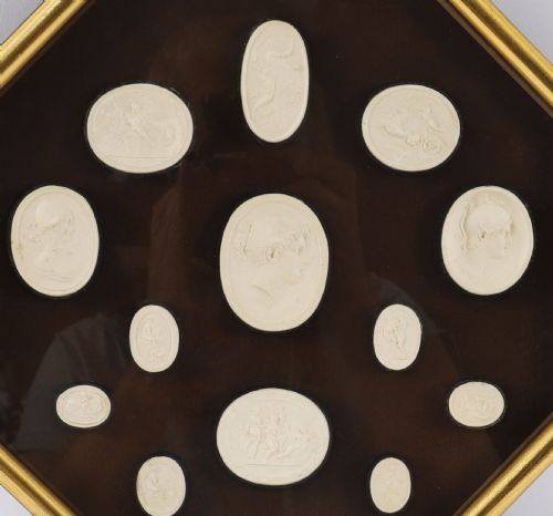 fig 2. A pair of octagonal giltwood framed wall displays featuring multiple cream plaster intaglio impressions mounted against a dark brown background.