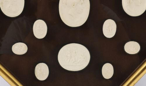 fig 3. A pair of octagonal giltwood framed wall displays featuring multiple cream plaster intaglio impressions mounted against a dark brown background.