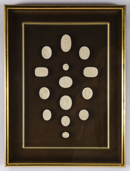 fig 1. A pair of dark velvet-lined gilt frames containing arrangements of white plaster classical intaglio cameos.