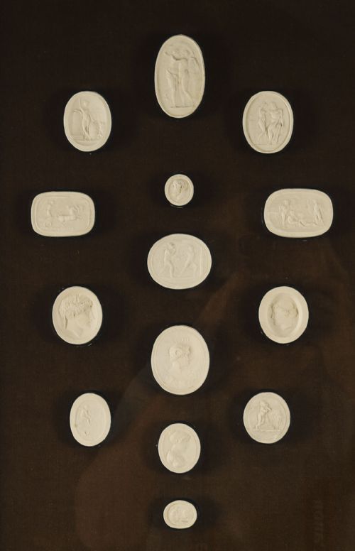 fig 2. A pair of dark velvet-lined gilt frames containing arrangements of white plaster classical intaglio cameos.