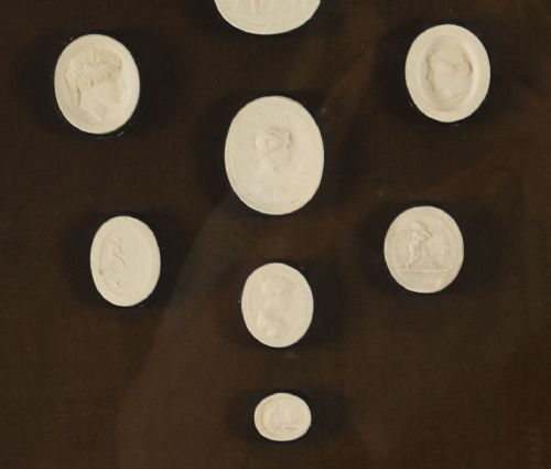 fig 3. A pair of dark velvet-lined gilt frames containing arrangements of white plaster classical intaglio cameos.