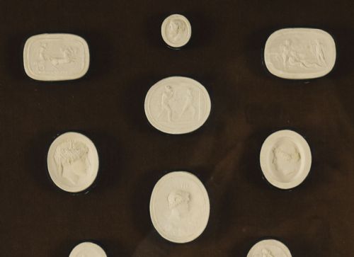 fig 4. A pair of dark velvet-lined gilt frames containing arrangements of white plaster classical intaglio cameos.