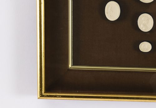 fig 6. A pair of dark velvet-lined gilt frames containing arrangements of white plaster classical intaglio cameos.