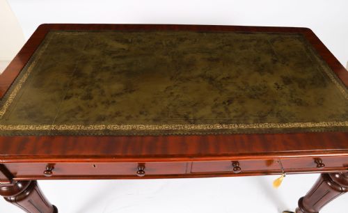 fig 3. A William IV mahogany writing desk featuring an inset green leather surface, two frieze drawers with knob handles, turned fluted legs, and brass castors.