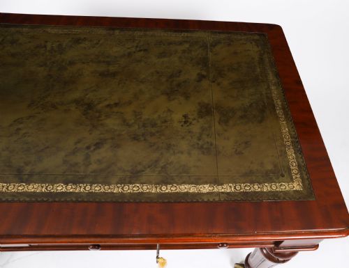 fig 4. A William IV mahogany writing desk featuring an inset green leather surface, two frieze drawers with knob handles, turned fluted legs, and brass castors.