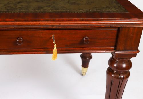 fig 5. A William IV mahogany writing desk featuring an inset green leather surface, two frieze drawers with knob handles, turned fluted legs, and brass castors.