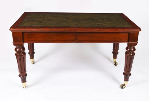 fig 6. A William IV mahogany writing desk featuring an inset green leather surface, two frieze drawers with knob handles, turned fluted legs, and brass castors.