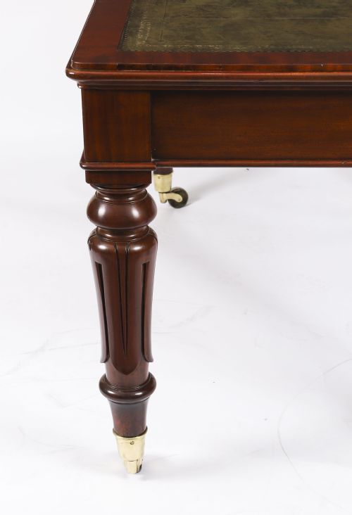 fig 7. A William IV mahogany writing desk featuring an inset green leather surface, two frieze drawers with knob handles, turned fluted legs, and brass castors.