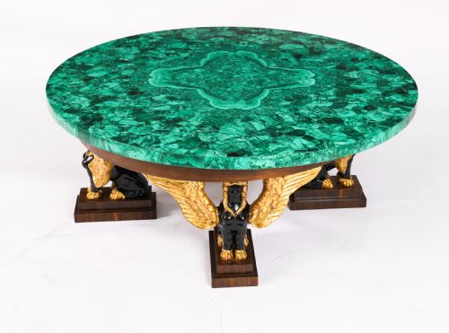 fig 3. A round coffee table featuring a green malachite stone veneer top supported by three carved ebonised and giltwood winged sphinx legs on dark plinth bases.