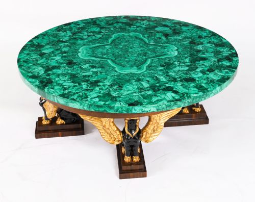 fig 4. A round coffee table featuring a green malachite stone veneer top supported by three carved ebonised and giltwood winged sphinx legs on dark plinth bases.