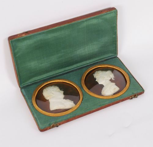 fig 1. A pair of white wax profile portrait reliefs of a man and a woman framed in circular brass bezels and displayed inside a green fabric-lined presentation case.
