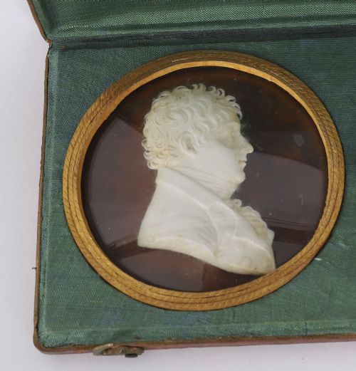 fig 3. A pair of white wax profile portrait reliefs of a man and a woman framed in circular brass bezels and displayed inside a green fabric-lined presentation case.