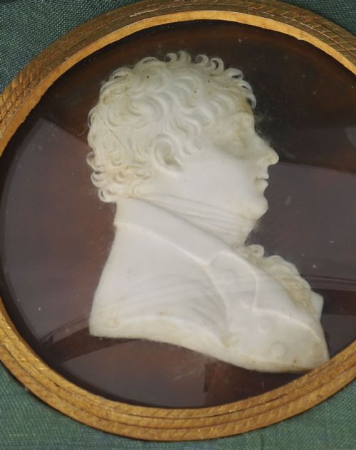 fig 4. A pair of white wax profile portrait reliefs of a man and a woman framed in circular brass bezels and displayed inside a green fabric-lined presentation case.