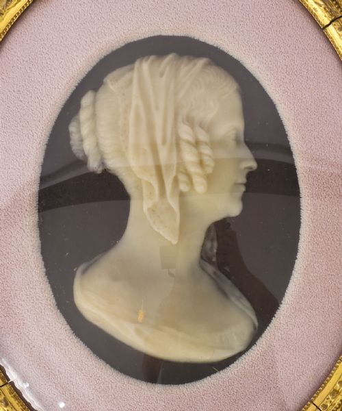 fig 1. A pair of oval gilt-framed 19th-century wax portrait reliefs featuring male and female profile busts set against dark backgrounds with pink fabric mounts.