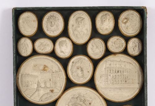 fig 3. An 18th-century boxed set of cream plaster Grand Tour intaglios showing classical profile portraits and Roman architectural scenes alongside an Italian manuscript index.
