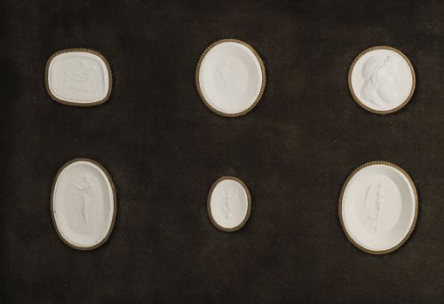 fig 1. A dark wooden moulding frame housing six white plaster classical intaglio impressions set against a dark brown velvet background.
