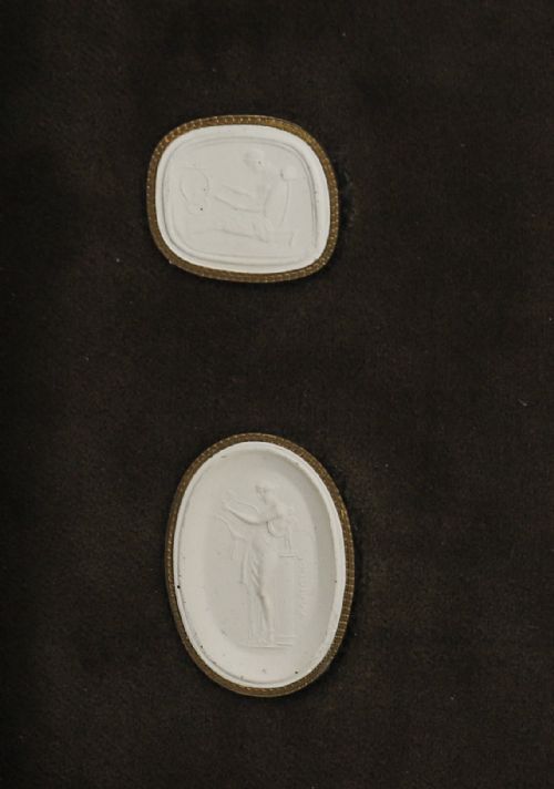 fig 2. A dark wooden moulding frame housing six white plaster classical intaglio impressions set against a dark brown velvet background.