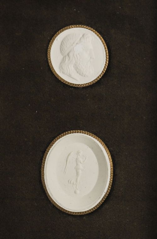 fig 4. A dark wooden moulding frame housing six white plaster classical intaglio impressions set against a dark brown velvet background.