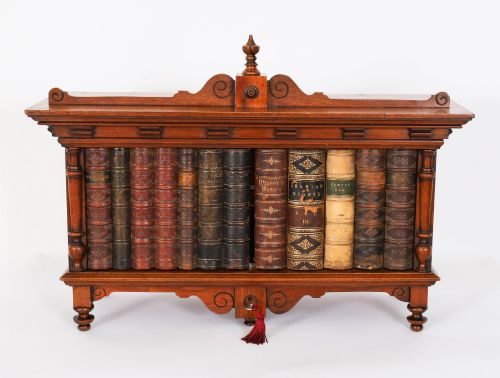 fig 1. An antique Victorian walnut tabletop collectors cabinet featuring a front styled with vintage book spines, turned columns, turned feet, and a central finial top.