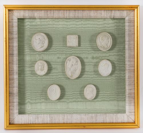 fig 2. A pair of framed displays containing white plaster intaglio relief medallions mounted on green patterned fabric inside gilt frames.