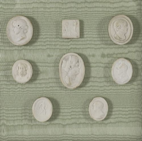 fig 3. A pair of framed displays containing white plaster intaglio relief medallions mounted on green patterned fabric inside gilt frames.