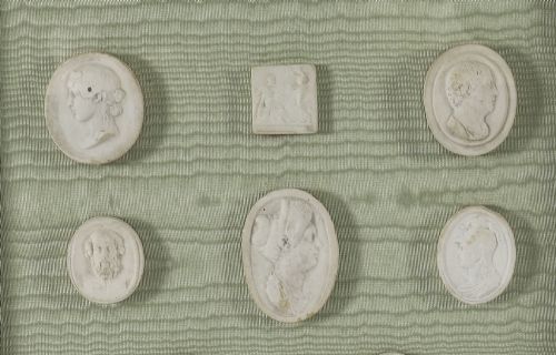 fig 4. A pair of framed displays containing white plaster intaglio relief medallions mounted on green patterned fabric inside gilt frames.