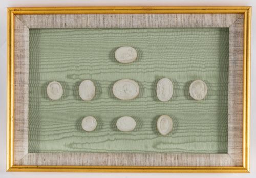 fig 7. A pair of framed displays containing white plaster intaglio relief medallions mounted on green patterned fabric inside gilt frames.