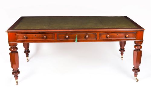 fig 1. A nineteenth-century mahogany partners writing table featuring a green leather inset surface, six drawers with turned knobs, and octagonal turned legs on brass castors.
