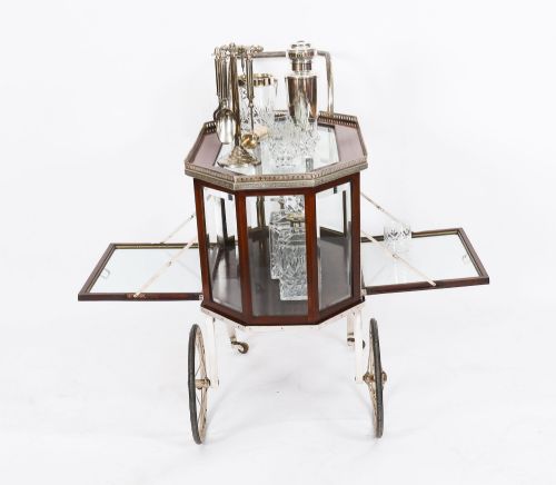 fig 4. An Art Deco drinks trolley featuring an octagonal glass top with metal gallery trim, wooden side frames, spoked wheels, and a drop-down door.