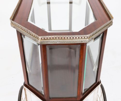 fig 6. An Art Deco drinks trolley featuring an octagonal glass top with metal gallery trim, wooden side frames, spoked wheels, and a drop-down door.