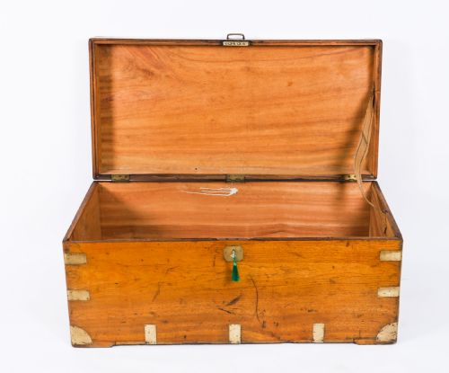 fig 2. A rectangular 19th-century warm brown camphorwood military campaign trunk featuring flush brass corner brackets, protective metal straps, side drop handles, and a central brass keyhole escutcheon.