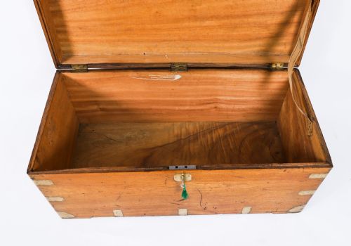fig 3. A rectangular 19th-century warm brown camphorwood military campaign trunk featuring flush brass corner brackets, protective metal straps, side drop handles, and a central brass keyhole escutcheon.