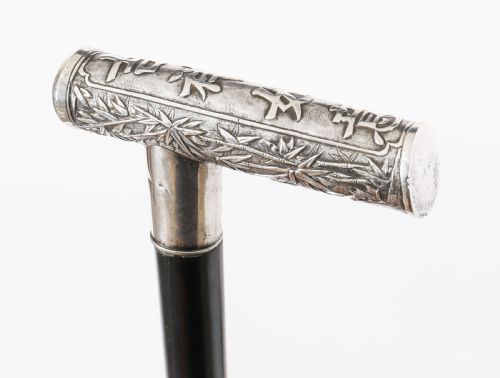 fig 1. An antique walking stick featuring a relief-carved silver handle decorated with prunus blossoms, set on a slender black ebonised wooden shaft with a brass tip.