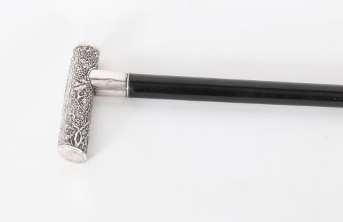 fig 3. An antique walking stick featuring a relief-carved silver handle decorated with prunus blossoms, set on a slender black ebonised wooden shaft with a brass tip.