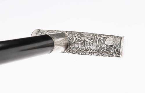 fig 5. An antique walking stick featuring a relief-carved silver handle decorated with prunus blossoms, set on a slender black ebonised wooden shaft with a brass tip.