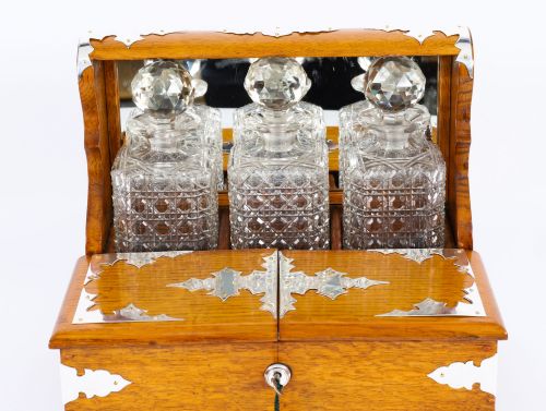 fig 2. An antique blonde oak tantalus featuring three square cut-glass decanters set against a mirror back, decorative silver-plated corner mounts, and a lower drawer with a key.