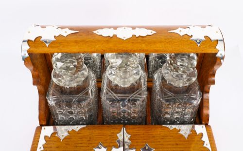 fig 3. An antique blonde oak tantalus featuring three square cut-glass decanters set against a mirror back, decorative silver-plated corner mounts, and a lower drawer with a key.