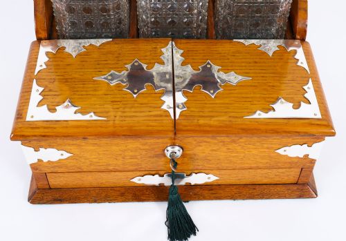 fig 4. An antique blonde oak tantalus featuring three square cut-glass decanters set against a mirror back, decorative silver-plated corner mounts, and a lower drawer with a key.