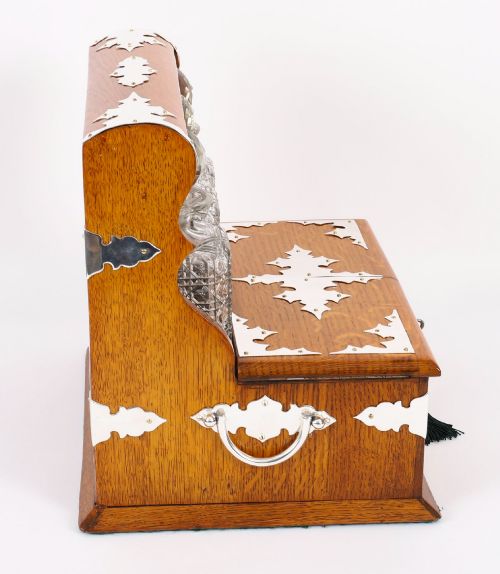 fig 6. An antique blonde oak tantalus featuring three square cut-glass decanters set against a mirror back, decorative silver-plated corner mounts, and a lower drawer with a key.