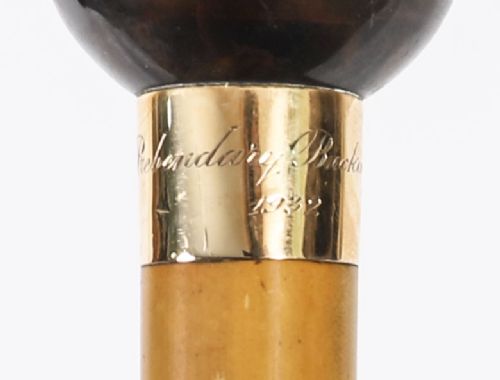 An antique Victorian wooden walking stick featuring a dark spherical pommel, an 18ct gold collar band, and a tapered brown shaft. View VI