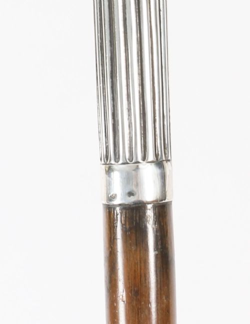 fig 2. An antique walking stick featuring a fluted silver crook handle mounted on a dark polished wooden shaft.