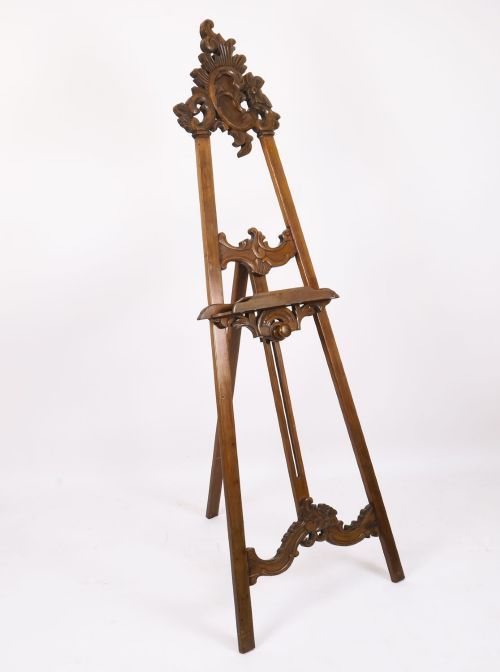 fig 3. A 19th-century carved walnut artist easel featuring an ornate Rococo Revival scrollwork crest and an adjustable ledge on a tripod frame.
